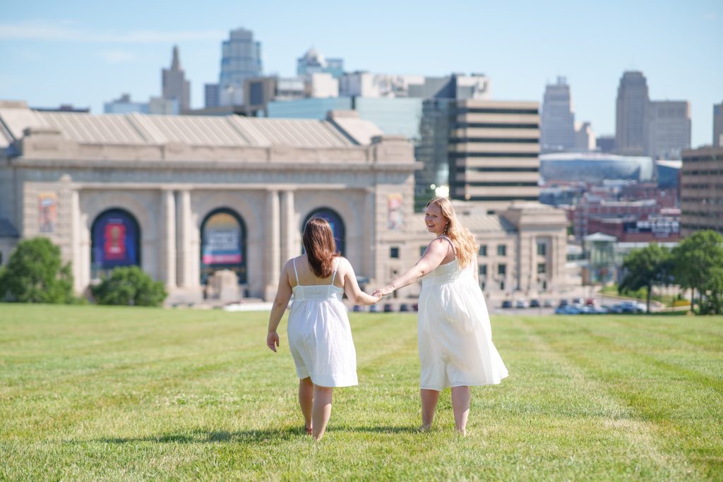 engagement session, engaged couple walking through grass, Kansas City skyline, downtown Kansas City